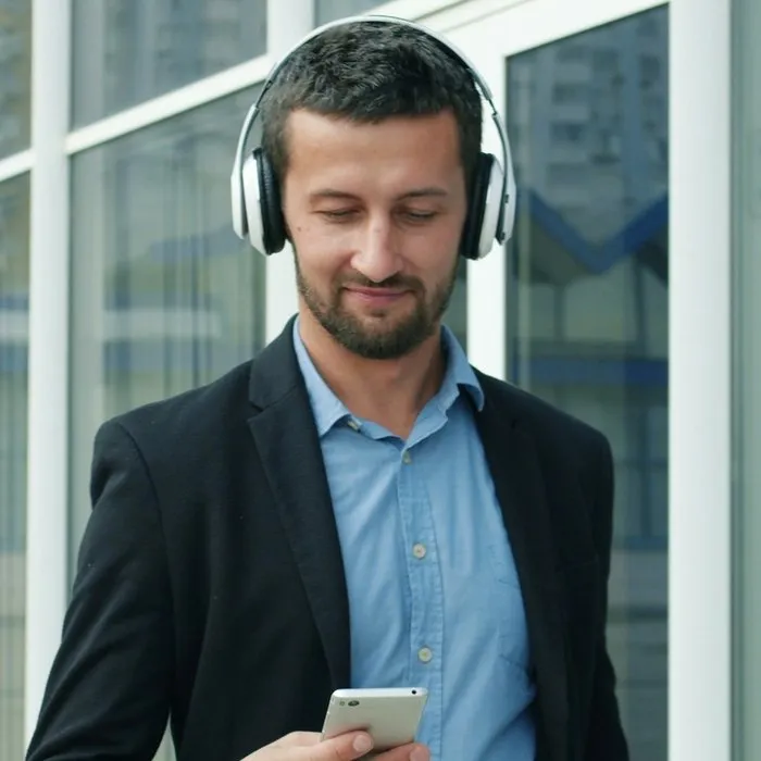 Een man met een hoofdtelefoon om zijn nek die op zijn telefoon leest