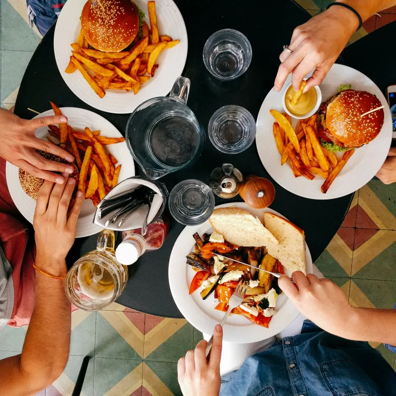 Mensen die hamburgers, frietjes en geroosterde groenten eten aan een ronde tafel, van bovenaf gezien